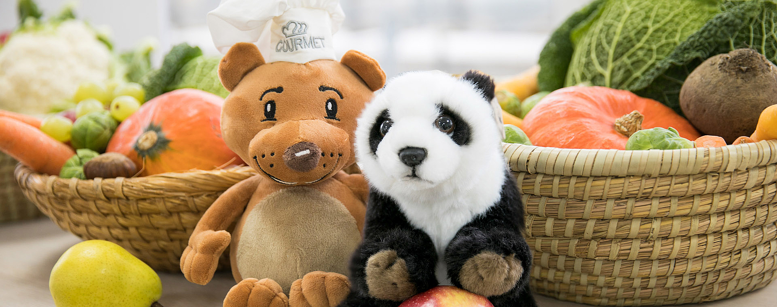 Das Gourmet Maskottchen Gourmelino und der WWF Pandabär vor Gemüse sitzend
