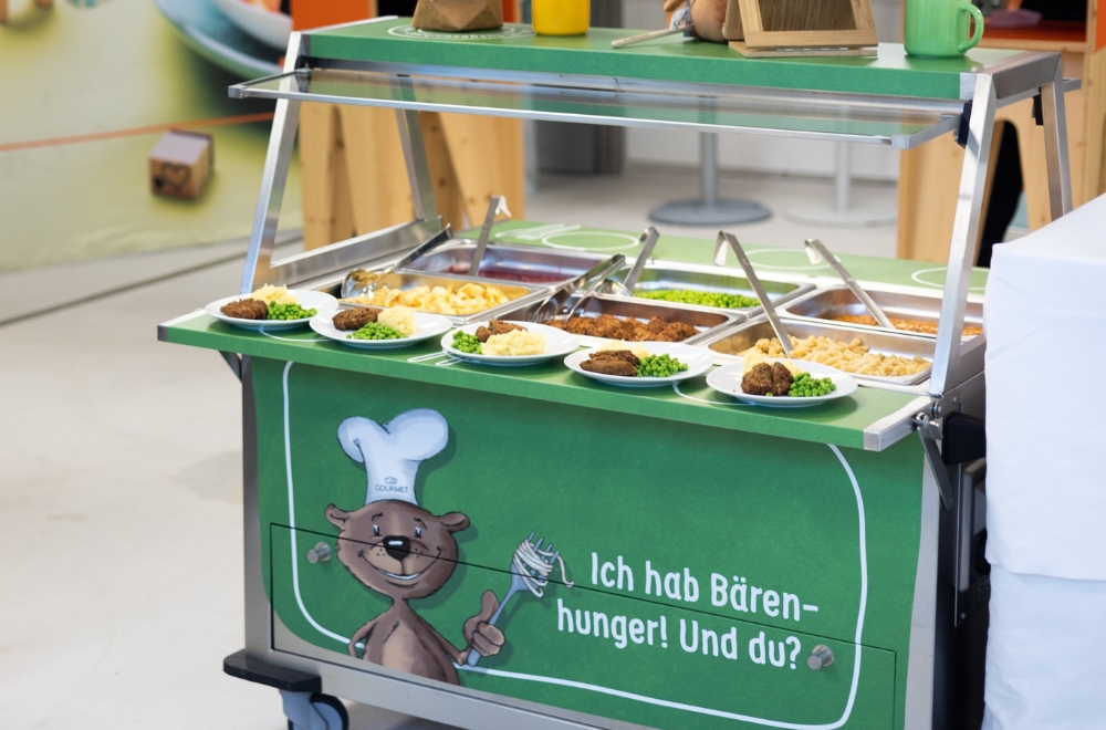 Die Speisen werden auf dem Buffetwagen serviert, der auch in Schulen zum Einsatz kommt und Kindern eine eigenständige Essensauswahl ermöglicht. 