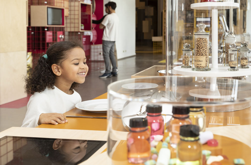 Kleines Mädchen schaut staunend auf Lebensmittel in der Ausstellung Foodprints